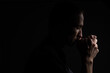 Close up of faithful mature man praying, hands folded in worship to god with head down and eyes closed in religious fervor. Black background. Concept for religion, faith, prayer and spirituality