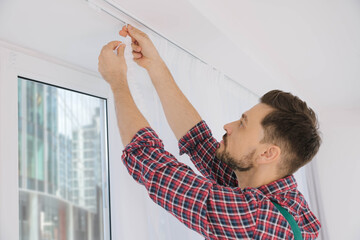 Poster - Worker in uniform hanging window curtain indoors, low angle view