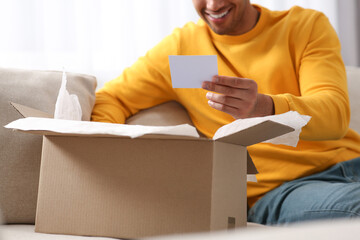 Wall Mural - Young man holding greeting card near parcel with Christmas gift, closeup