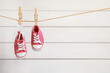 Cute pink baby sneakers drying on washing line against white wall. Space for text