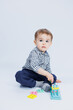 © DSMT - A cute little boy in a checkered shirt sits on a white background and plays with wooden educational toys. Ecological wooden toys for children