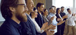 © Studio Romantic - Audience applauding speaker after successful presentation at business conference or office meeting. Team of happy people standing in row, smiling and clapping hands all together. Side, profile view