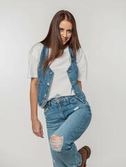 Sticker - Stylish beautiful young woman model with a smile in fashionable jeans clothes with a denim vest, T-shirt and jeans poses and having fun on a white background in the studio