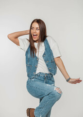 Sticker - Beautiful emotional positive woman with funny emotions in fashionable denim outfit with a jeans vest, white T-shirt and jeans on a white background in the studio