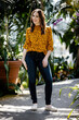 Beautiful smiling brunette Caucasian female in a leopard print shirt and blue jeans surrounded by greenery 