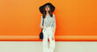 © rohappy - Portrait of beautiful young woman with handbag wearing white striped shirt, black round hat on orange background