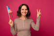 Ecstatic mid age woman is showing V gesture and holding a small USA flag.