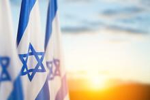 Israel Flags With A Star Of David Over Cloudy Sky Background On Sunset. Banner With Place For Text.