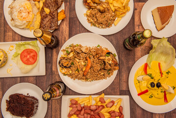 Wall Mural - A set of Peruvian food dishes with papas a la huancaina in the center, a quesillo, steaks with rice and plantains, arros chaufa and drinks on a brown table