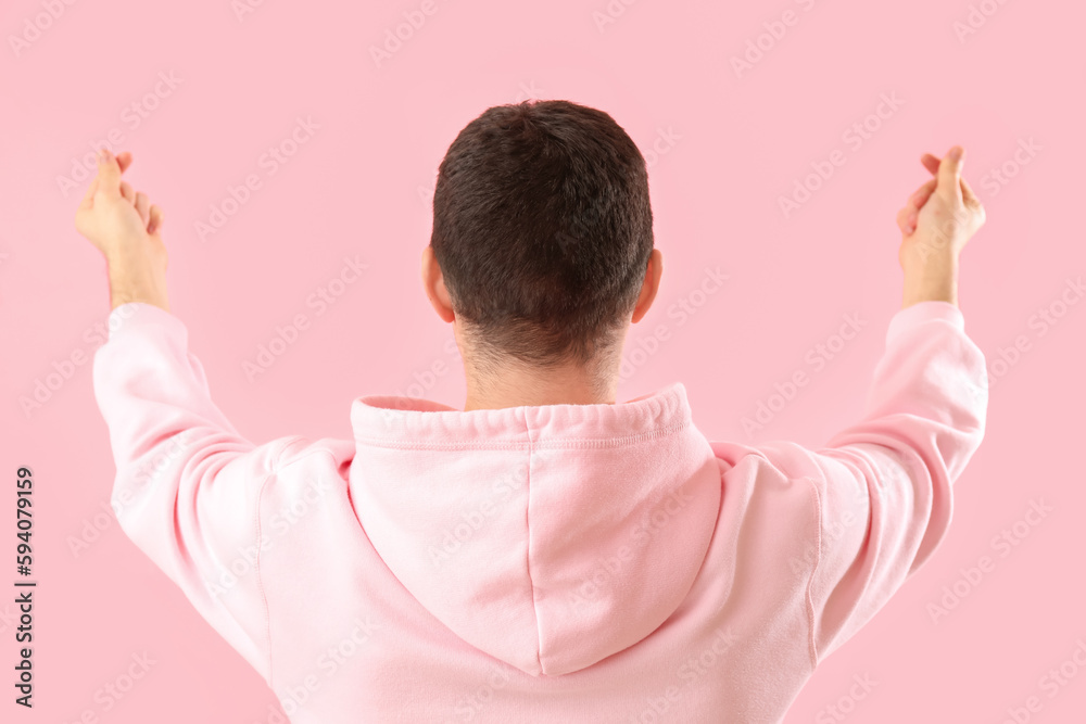 Young man making heart with his fingers on pink background, back view