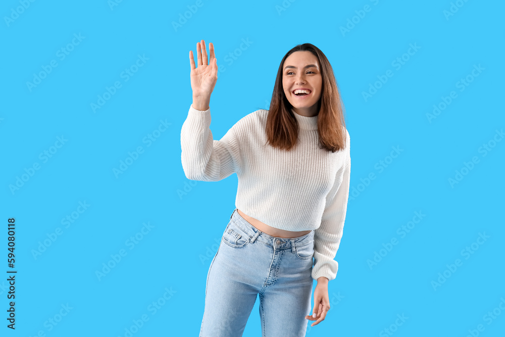 Beautiful young woman waving hand on light blue background