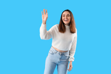 Wall Mural - Beautiful young woman waving hand on light blue background
