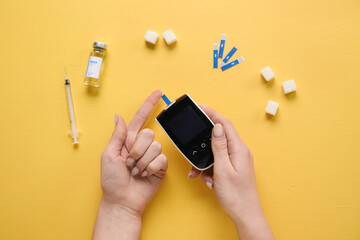 Wall Mural - Diabetic woman using glucometer on yellow background