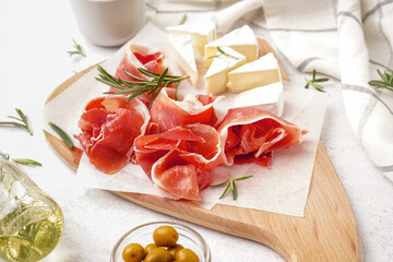 Wooden board with tasty jamon slices on light background