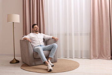 Wall Mural - Happy man resting on armchair near window with beautiful curtains at home. Space for text