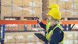 © Monster Ztudio - Warehouse workers holding digital tablet checking inventory management packaging boxes. Two staff wearing vest and safety helmet and walking count the box goods on shelves at storehouse