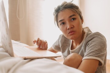 Wall Mural - Serious asian woman working with her laptop in the bedroom.