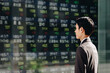 ビジネス街の株価ボードを見てNISAでの運用を考える30代の日本人のビジネスマンの男性の横顔