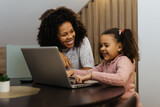 Fototapeta Londyn - Smiling african american mother and daughter using laptop at home