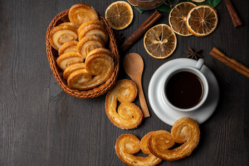 Overhead view of puff pastry sweets in basket with cup of coffee, dried oranges and cinnamon sticks, horizontal, with copy space