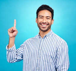 Poster - Point, excited and portrait of Asian man on blue background for news, information and announcement. Advertising, studio mockup and happy male pointing for copy space, promotion and showing gesture