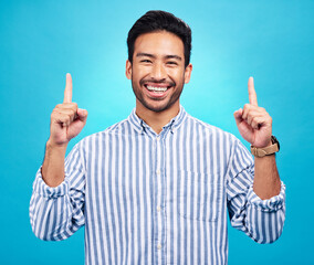 Poster - Point, happy and portrait of Asian man on blue background for news, information and announcement. Advertising, studio mockup and face of excited male pointing for copy space, promo and showing sign