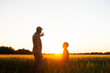 © Acronym - Farmer and his son in front of a sunset agricultural landscape. Man and a boy in a countryside field. Fatherhood, country life, farming and country lifestyle concept.