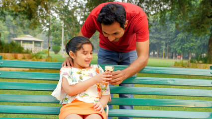 Wall Mural - Loving father giving delicious ice cream to his daughter - happy family moments. Shot of a handsome dad and his small child spending their leisure time in a beautiful park