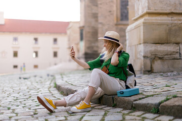 Poster - Young woman travel alone in old city centre, sitting and taking selfe.