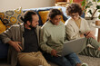 © pressmaster - African American teenage girl using laptop together with her foster parents while they sitting on the floor in the room
