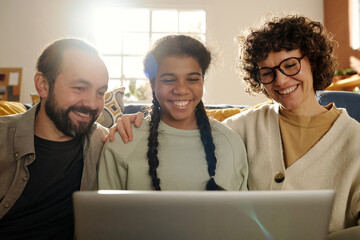 Wall Mural - Happy family with adopted child having video call on laptop, they talking and smiling sitting in the living room