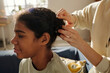 © pressmaster - Close-up of mother making hairstyle to her African American adopted daughter preparing her for school