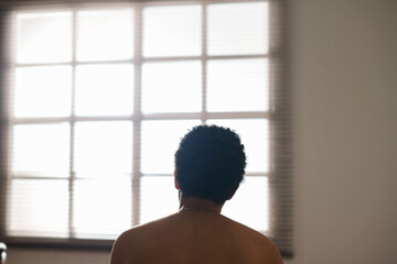 Rear view of lonely sad man looking at window sitting alone in the room