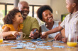 © Monkey Business - Family Shot With Grandparents And Grandchildren Doing Jigsaw Puzzle On Table At Home