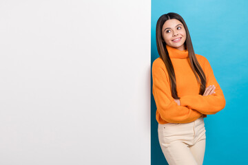 Poster - Photo of cute girl long hairstyle dressed knit turtleneck hold arms crossed look at board empty space isolated on blue color background