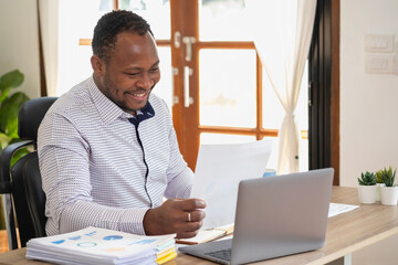 Wall Mural - African American businessman of black descent sits smiling and doing financial reports and studying annual profit analysis An accountant checking the financial status of the company is in the office.