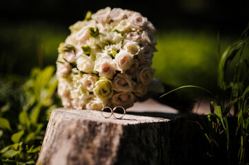 Wall Mural - Two golden wedding rings on a stump, a bride's bouquet of flowers in the background