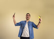 © Moon Safari - Male customer with credit card and smart phone pumping fists and screaming ecstatically over beige background. Happy young man shouting after receiving coupons for online shopping and paying