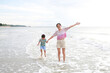 © zilvergolf - Happy Asian mom and son at tropical sand beach with waving hands. Happy family mother and little boy having fun in summer holiday.
