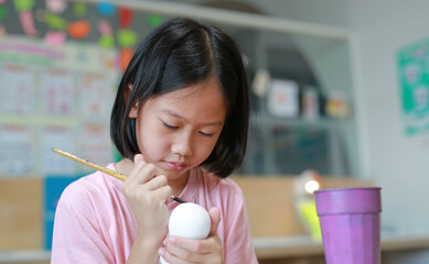 Wall Mural - Asian girl painting a doll with watercolor. Kid with water color painting activity.