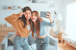 © oatawa - Two happy asian women blogger shooting social media stories or video calling in mobile app and enjoying rest in living room at home. selfie