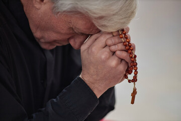 Wall Mural - Close-up of senior man with grey hair praying with rosary beads in his hands