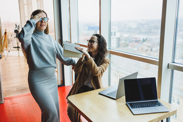 Wall Mural - A pregnant woman is working in the office with a colleague on a new project, they are looking at a laptop. The work of female managers in a modern, spacious office