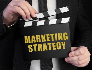 Poster - A businessman holds up a ?lapperboard with text MARKETING STRATEGY