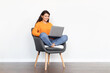 © Prostock-studio - Happy pretty indian woman sitting in armchair, using laptop
