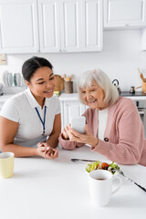 Wall Mural - happy senior woman using smartphone near multiracial social worker at home.