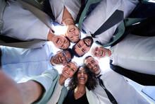 Multiethnic Group Of Work Colleagues Embraced In Circle, Face Down Taking A Selfie Smiling And Looking At The Camera. POV Business People Doing Team Building. 
