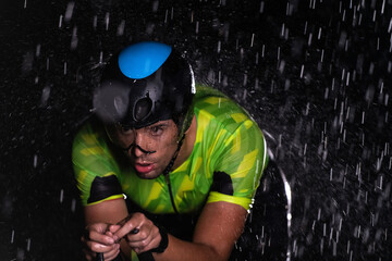 A triathlete braving the rain as he cycles through the night, preparing himself for the upcoming marathon. The blurred raindrops in the foreground and the dark, moody atmosphere in the background add