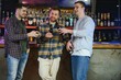 © Serhii - Three young men in casual clothes are smiling, holding bottles of beer while standing near bar counter in pub