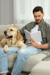 Poster - Man reading book on sofa near his cute Labrador Retriever at home